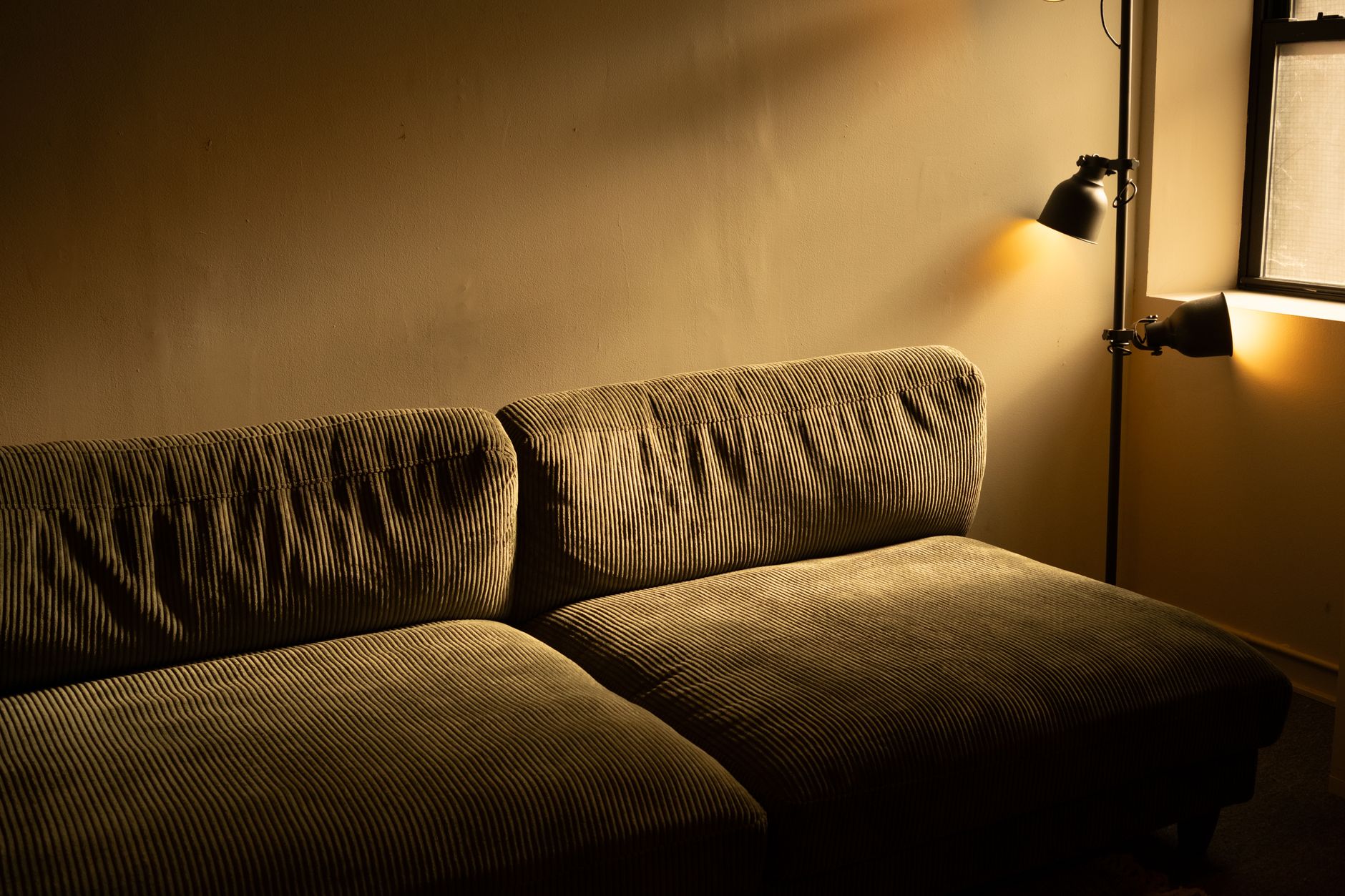 Woonkamer in warm avondlicht met een ribstof bank tegen een lichte wand